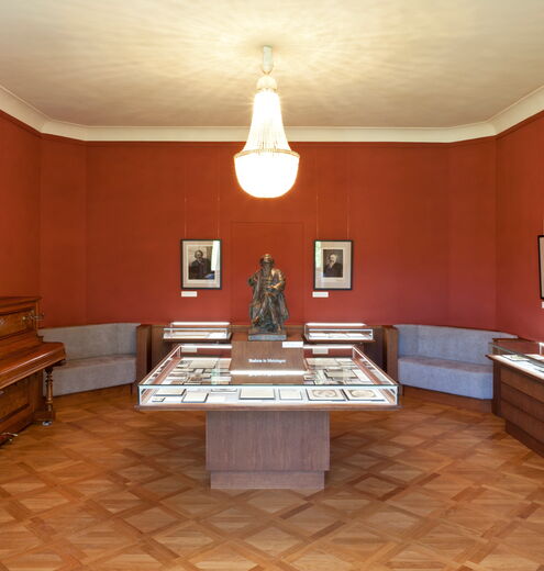 Innenaufnahme Brahms-Gedenkstätte im Schloss Altenstein mit Brahms-Statue, Klavier, Kronleuchter und Ausstellungsvitrinen