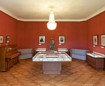 Innenaufnahme Brahms-Gedenkstätte im Schloss Altenstein mit Brahms-Statue, Klavier, Kronleuchter und Ausstellungsvitrinen